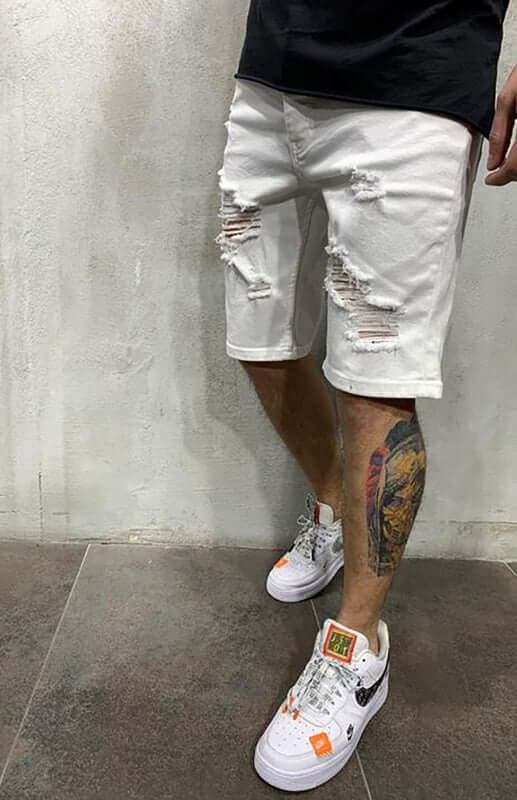 Man wearing Averra ripped white short jeans, styled with trendy sneakers, perfect for streetwear fashion.