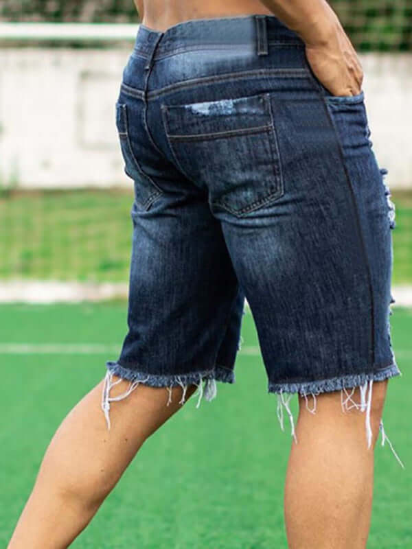 Men's streetwear denim in slim fit, showing back view of fashionable ripped shorts on a grassy field.